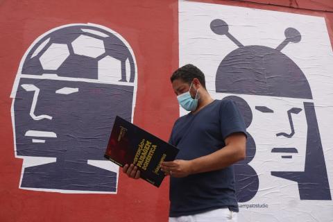 Artista com livro e colagens ao fundo #paratodosverem