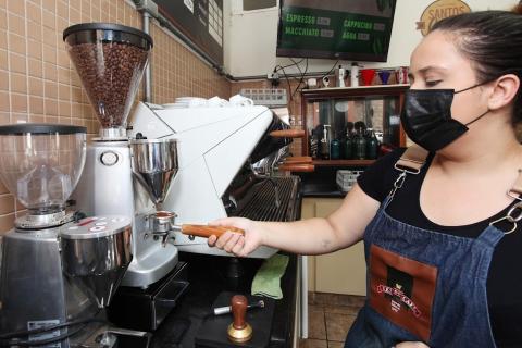 mulher usando avental prepara café em máquina. #paratodosverem