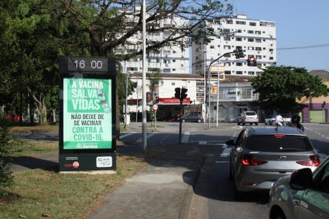 relógio marca hora em canteiro central à esquerda. Carros estão parados na pista à direita. #paratodosverem