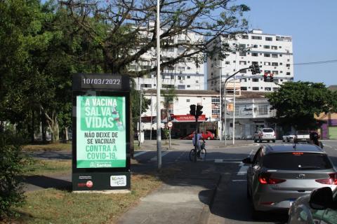 relógio marca data em totem em canteiro central à esquerda. Carros estão parados à direita na via. #paratodosverem