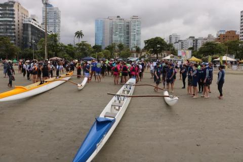 canoas na areia antes da largada. Ao fundo, as equipes com atletas. #paratodosverem