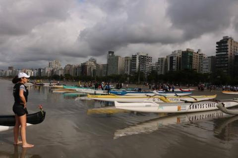 canoas estão na beira d'água. à esquerda, uma mulher olha para as canoas. #paratodosverem