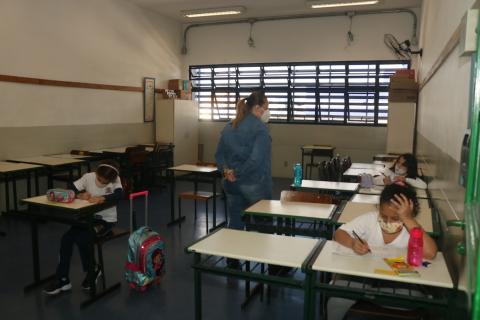 alunos em sala, distantes uns dos outros. Professora está em pé. #paratodosverem