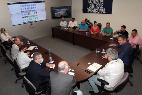 reunião no centro de controle operacional, com várias pessoas sentadas numa grande mesa em formato de letra U. #paratodosverem