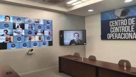 sala com painel ao fundo demonstrando uma reunião virtual. #paratodosverem