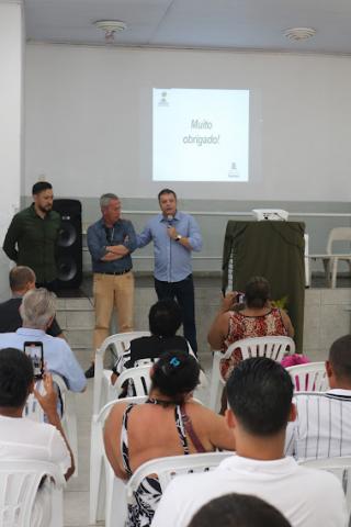 prefeito fala aos moradores. Ele está em pé, ao microfone, pessoas estão sentadas. #pratodosverem