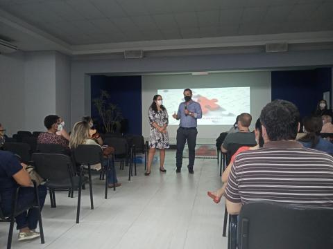 duas pessoas em pé em uma sala e outras sentadas. #paratodosverem