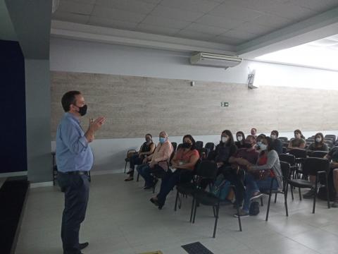homem está em pé falando a várias pessoas sentadas. #paratodosverem