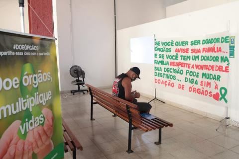 homem sentado lê panfleto com cartaz e faixa sobre doação ao redor