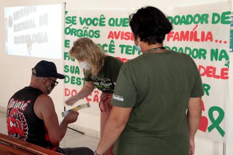 mulher mostra panfleto e faixa sobre doação atrás #paratodosverem