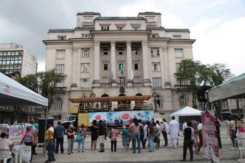 pessoas e palco montado na praça com prefeitura ao fundo #paratodosverem