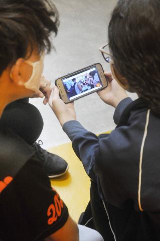 #pracegover dois alunos assistem a vídeo em ceclular