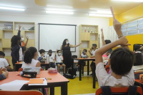 crianças sentada em circulo na classe, com algumas com a mão levantada #paratodosverem