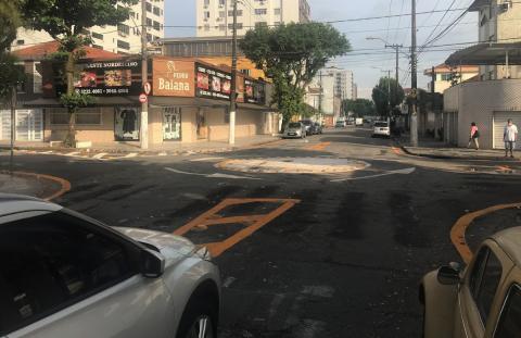 Carro percorre a rua para entrar na rotatória ao fundo. #Paratodosverem