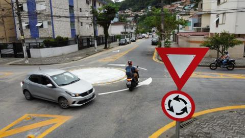 minirrotatória com carro e moto circulando. Em primeiro plano, placa vertical indicativa do equipamento. #paratodosverem