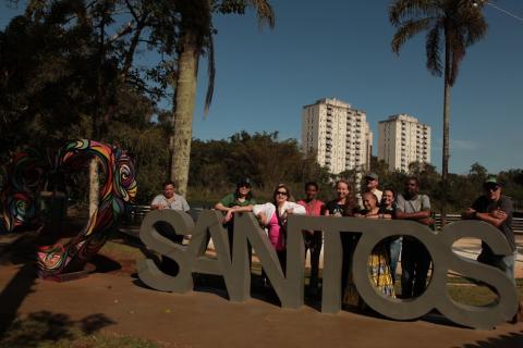 grupo de pessoas posa para foto atrás de monumento amo santos em uma praça. #paratodosverem