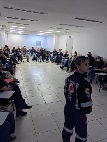 agente uniformizada do samu fala a grupo de pessoas sentadas. #paratodosverem