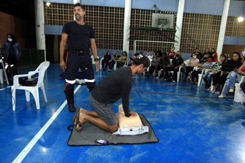 morador está ajoelhado no chão e apoia as mãos sobre tronco de boneco de borracha para simular massagem cardíaca. #paratodosverem