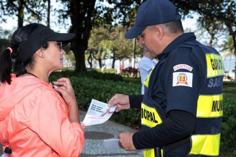 guarda municipal entrega folheto para mulher que está atenta ao que o agente fala. #paratodosverem