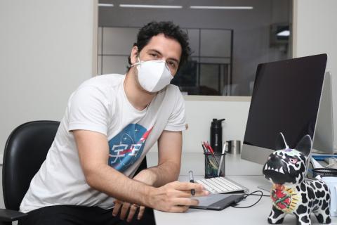 O programador Héctor está sentado diante de um monitor. Ele posa para a foto. #paratodosverem