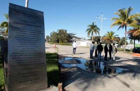 Placa em primeiro plano e ao fundo pessoas conversando e olhando para obra. #paratodosverem