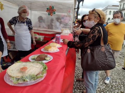 Mulher pega comida em barraca, com vários alimentos em cima da mesa #paratodosverem