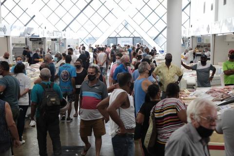 diversas pessoas circulam por um corredor do mercado. Não é possível ver os balcões de venda. #paratodosverem