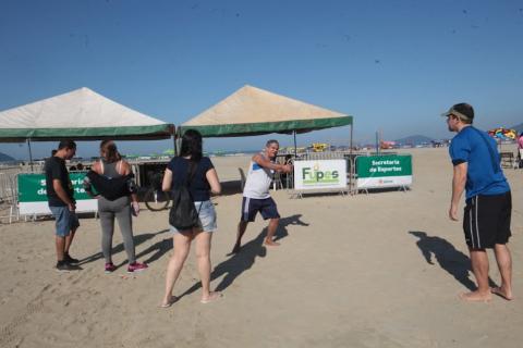 servidores estão em pé na faixa de areia diante de barracas. #paratodosverem