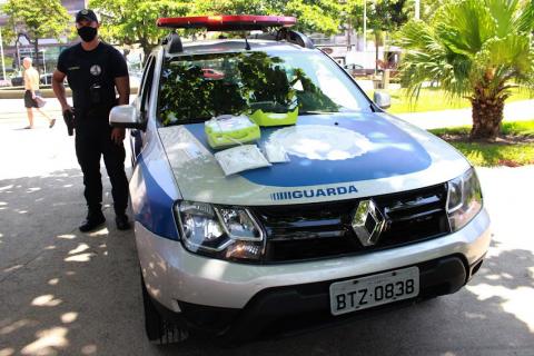 guarda está em pé ao lado de viatura sobre a qual há dois desfibriladores. #paratodosverem