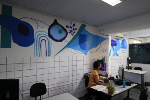 Mural com temas marinho e mulher trabalhando no computador. #pracegover