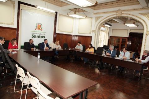 prefeito e secretários reunidos com representantes de entidades. Todos estão sentados em torno de uma mesa em forma de letra U. #paratodosverem