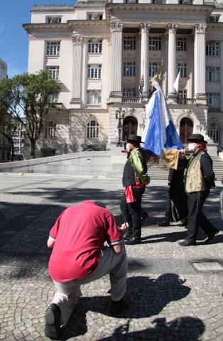 rapaz se ajoelha diante de imagem de santa #paratodosverem