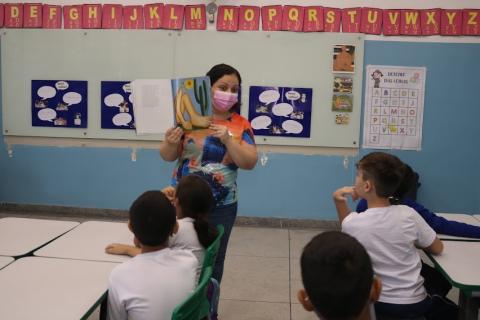 professora segura livro com figura de Abaporu. Crianças observam