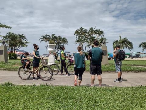 ciclistas param no meio do jardim da orla para observar busto de Lidia Federici. #paratodosverem