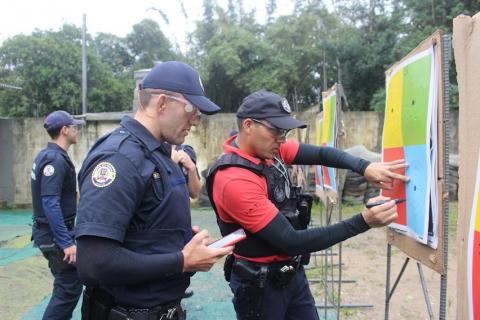 guarda está ao lado de instrutor que faz marcação com caneta em alvo colorido. #paratodosverem