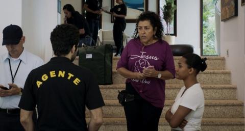 cena de três verões. Agente policial está de costas. Mulher está em escada conversando com ele. Há outra mulher ao lado. #paratodosverem