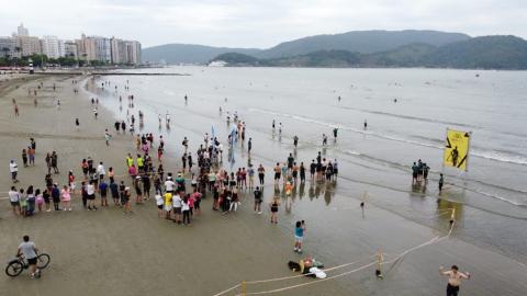 Imagem aérea da concentração de atleta e público na Praia da Aparecida. #pracegover