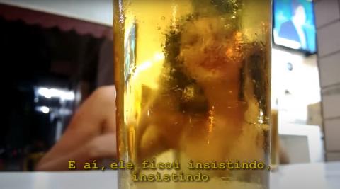 Imagem de uma pessoa sentada é refletida em um copo cheio de líquido. #paratodosverem