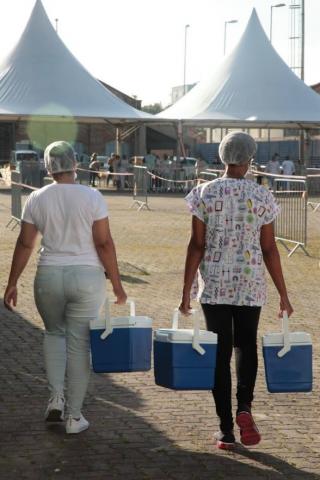 Mulheres carregam coolers com vacinas. #Paratodosverem