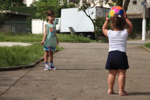 Duas crianças brincam de bola em praça. #Paratodosverem