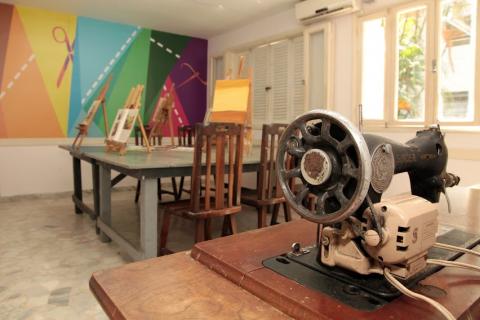 sala de artesanato e arte, com tripés para pintura de quadros. Em primeiro plano, uma mesa de costura com uma antiga máquina singer. #paratodosverem