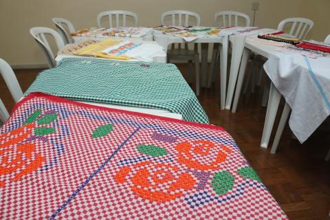 sala de artesanato com várias toalhas bordadas sobre as mesas. #paratodosverem