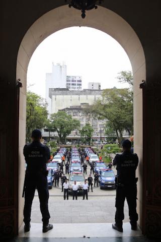 vista das viaturas na praça de dentro da prefeitura, com destaque para o acesso principal do prédio e seu formato curvo. Na entrada da prefeitura, dois homens estão de costas. Ao fundo, no chão da praça, os  veículos. #paratodosverem