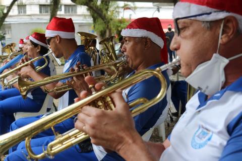 Apresentação de banda de sopro, com músicos usando gorro de papai noel. #paratodosverem