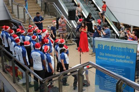 coral está formado para apresentação. Todos os integrantes usam gorro de papai noel. Ao lado deles há um banner onde se lê 3 de dezembro, Dia Internacional da Pessoa com Deficiência. #paratodosverem