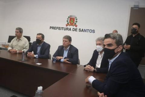 o ninistro sentado no CCO ao lado do prefeito e outras autoridades. Ao fundo, na parede, está afixado brasão de santos e onde se lê prefeitura de santos. #paratodosverem