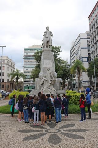 crianças estão em torno do monumento a Braz Cubas. #paratodosveem