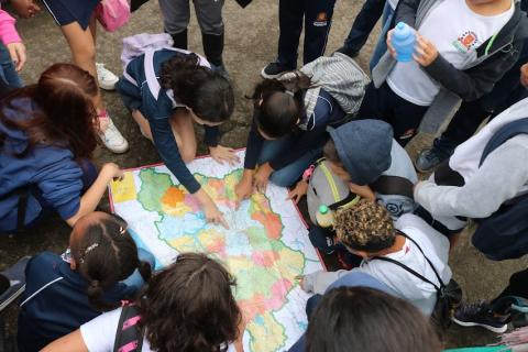 crianças estão no chão olhando e apontando para mapa. #paratodosverem
