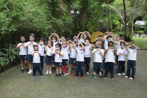 crianças posam juntas para foto, no jardim do casarão, fazendo gesto de coração com as mãos. #paratodosverem