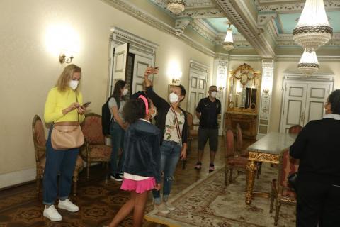 Turistas observam e tiram fotos do salão nobre. #pracegover